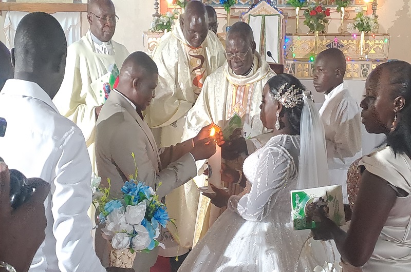 Angelo lights a holy candle held by his wife Margaret in the presence of Fr. Alule, fellow Priests and other witnesses in Christ the King Church Arua on Saturday. Photo Credit, Andrew Cohen Amvesi